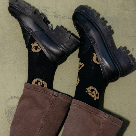 Model wearing pretzel socks with brown pants and black shoes.