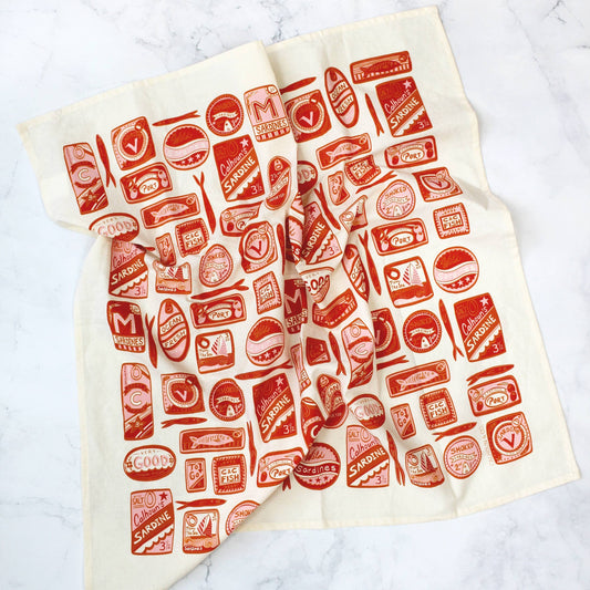 White tea towel designed with variously shaped, red, tin sardine cans.  