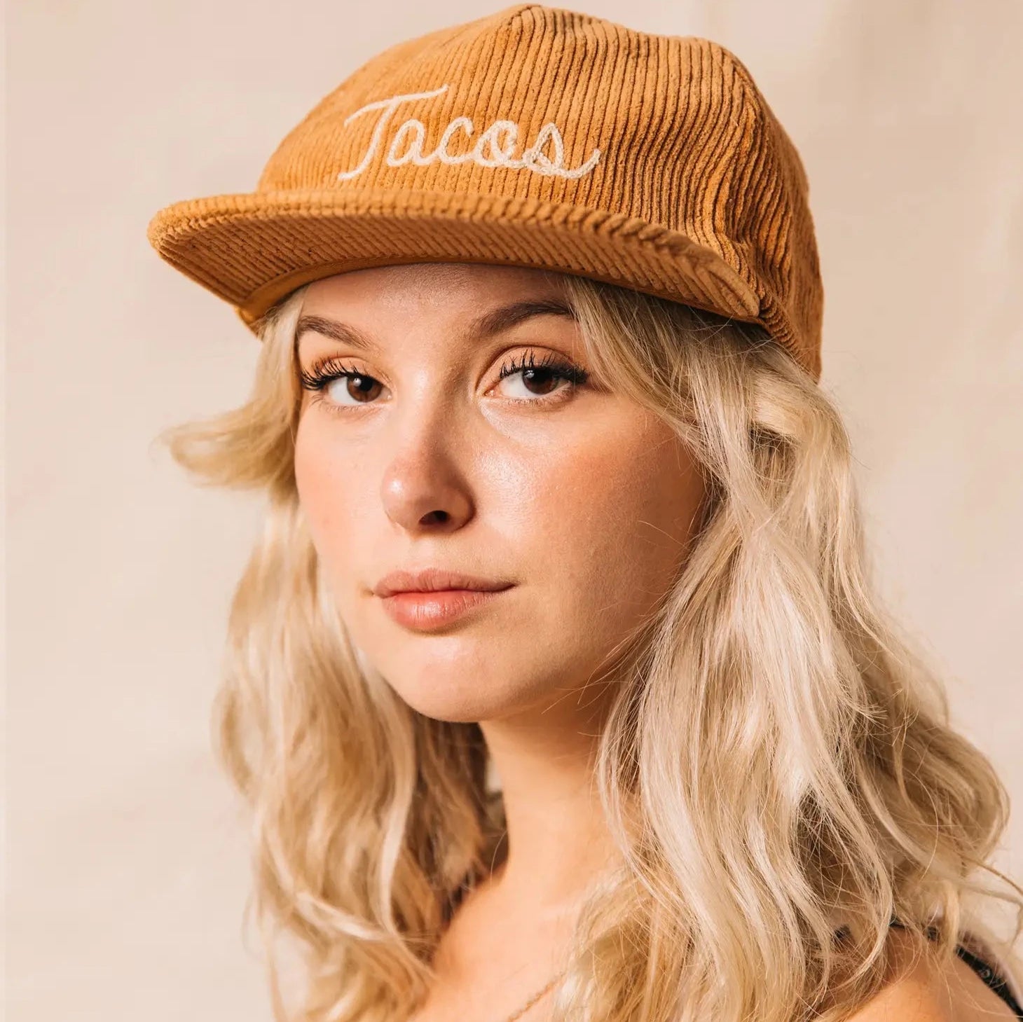 Tan colored, corduroy cap with "Tacos" embroidered on the front on model 