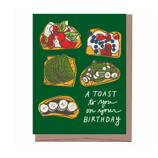 Greeting card with text "A TOAST to you on your BIRTHDAY" and illustration on vibrant green background. Illustration features five different "toasts" (ie. open-faced sandwiches) - cucumber and veggie toast, avocado toast, mixed berries and cream cheese toast, caprese toast, Nutella and bananas toast. 