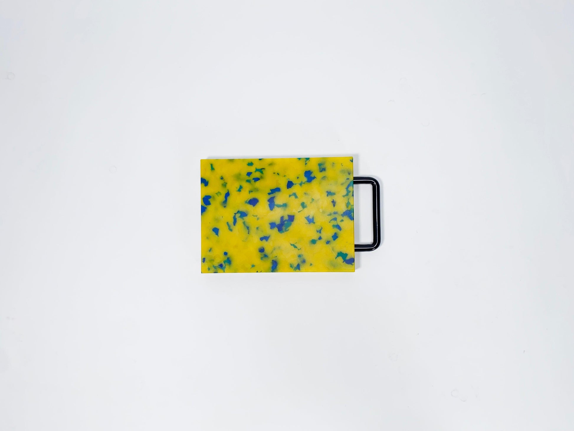 Small yellow cutting board with blue confetti and black handle 