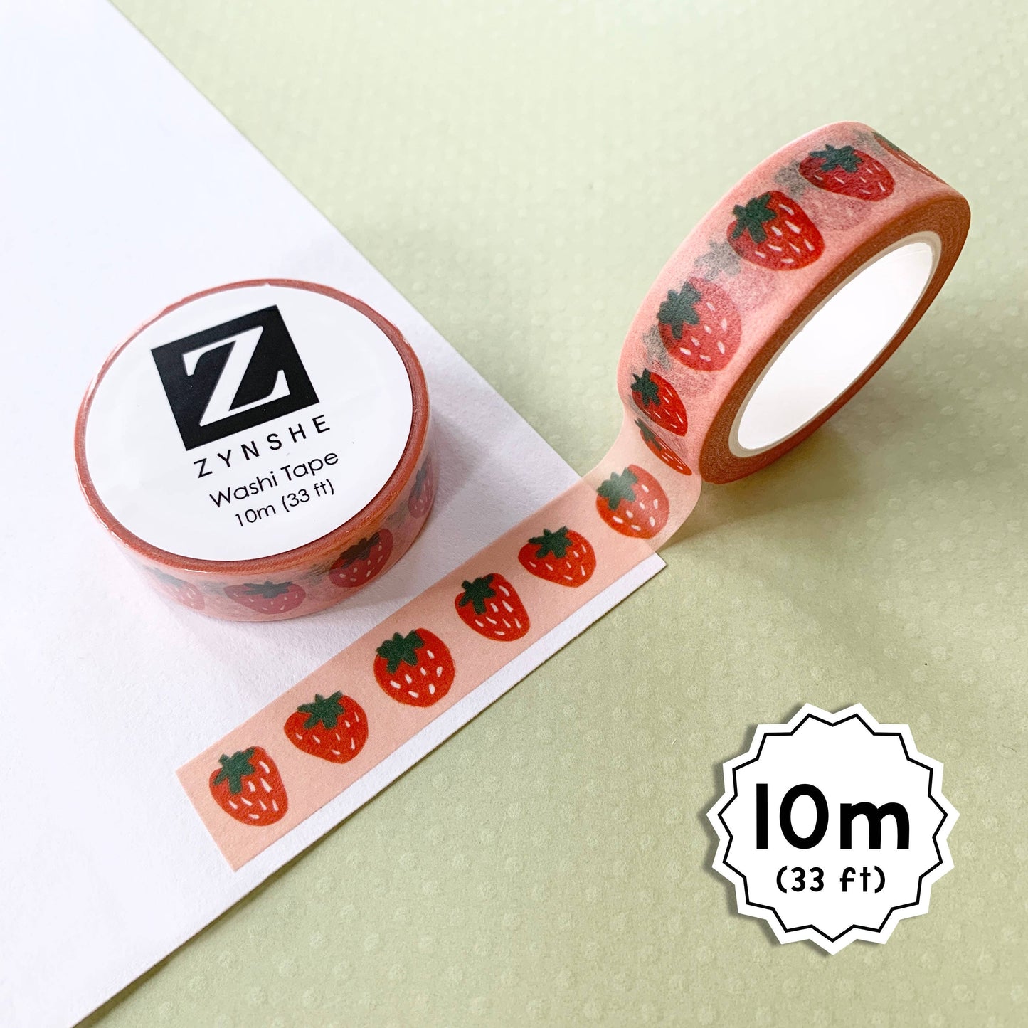 Photo of washi tape with strawberries print. Image on tape is of red strawberries with white seeds and green leaves on simple pink background.