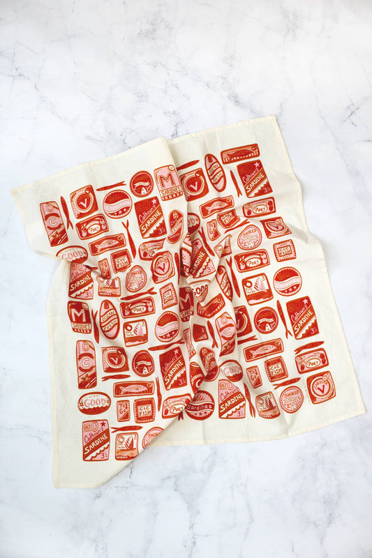 White tea towel designed with variously shaped, red, tin sardine cans.  