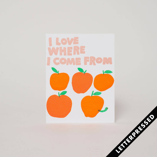 Greeting card that reads "I love where I come from" and has 5 apples on it, the last one also having a worm come out of it 