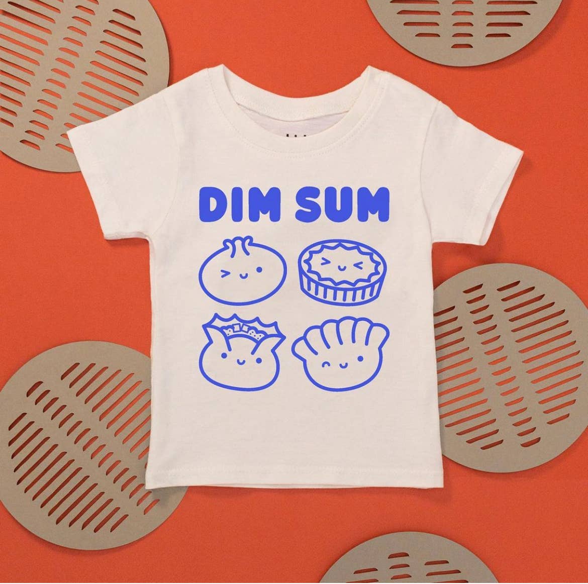 White kids tee with illustrations of various dim sum on it, printed in blue ink and text that reads "Dim Sum" across the chest 