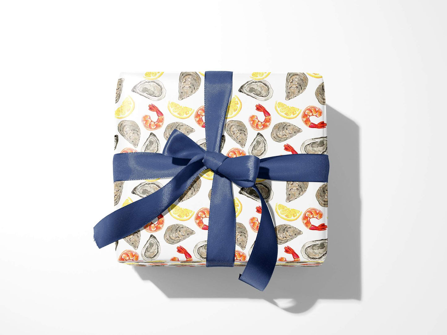 Box wrapped in wrapping paper designed with oysters, shrimp and lemon wedges all over and blue ribbon tied into a bow on top 