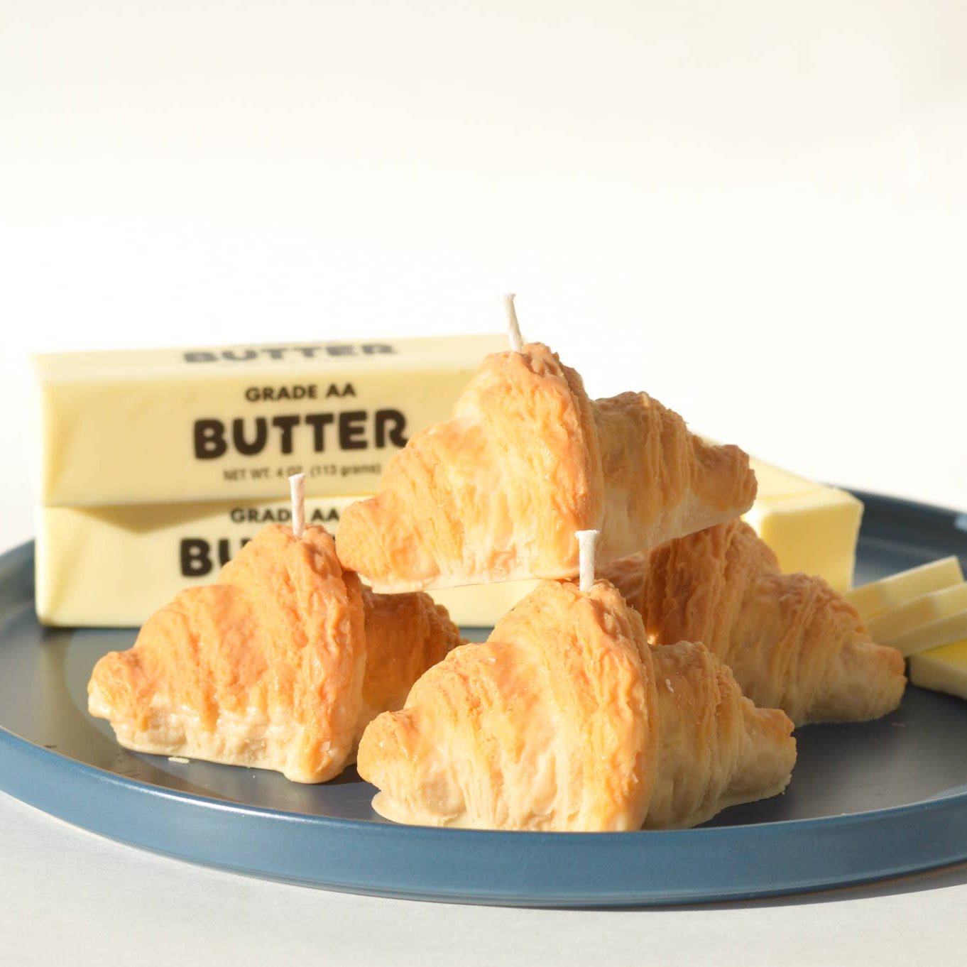 Pile of four croissant candles on a plate next to slabs of butter.