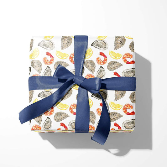 Box wrapped in wrapping paper designed with oysters, shrimp and lemon wedges all over and blue ribbon tied into a bow on top 