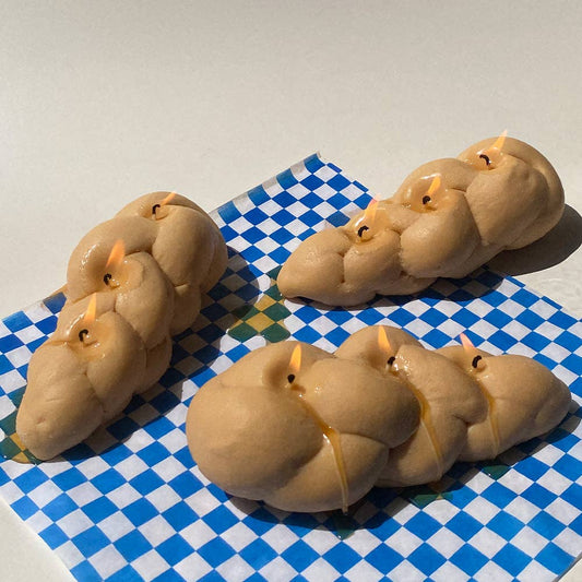 3 candles that look like Challah bread. Each candle has 3 wicks and are lit.