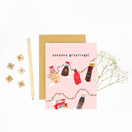 Holiday card with various asian seasoning sauces on it including kewpie mayo, soy sauce, sriracha, sesame oil, gochujang and oyster sauce. Black text reads "seasons greetings" 